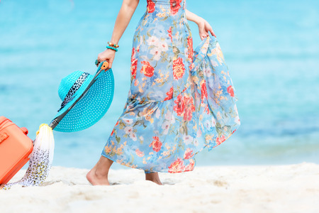 Travel Plan. Hand women traveler holding orange luggage walking on the beach. Traveler and Tourism planning trips summer vacations with Traveler's accessories summertime. Summer Conceptの写真素材