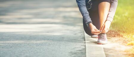 Running woman tying laces of running shoes before jogging through the road in the workout nature...
