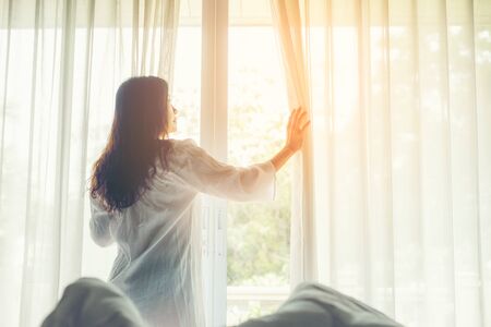 Lifestyle Women open window after get up the white bed in morning sunrise relax mood in the bedroom. Lifestyle Concept.の写真素材