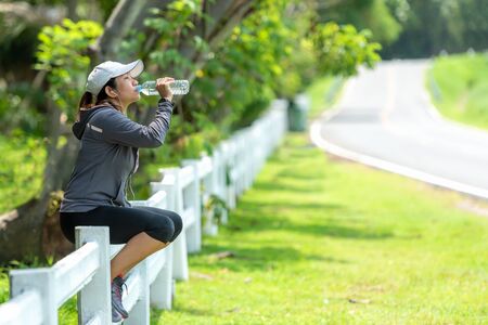 Healthy athletic asian woman is drinking pure water from the bottle refreshing herself after exercise in the nature park. Healthy and Lifestyle Conceptの写真素材