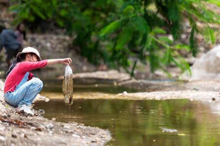 Asian girl collecting garbage and plastic on the river to dumped into the trash.  Save environment Concept.の写真素材