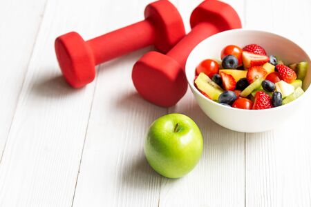 Healthy lifestyle for women diet with fresh fruits salad and dumbbells sport equipment, fruit healthy green apples on wooden.  Healthy Concept.の写真素材