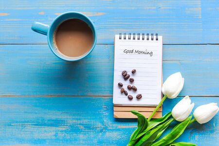 Cozy winter relax time.  Cup of hot coffee with write note on paper and lily flower on the blue wood background in morning sunny day. Lifestyle conceptの写真素材