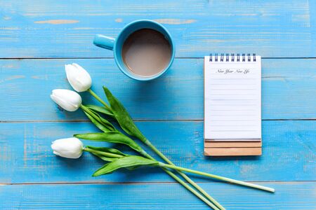 New Year and New Life.  Cozy winter relax time.  Cup of hot coffee with write note on paper and flower on the blue wood background in morning sunny day. Lifestyle conceptの写真素材