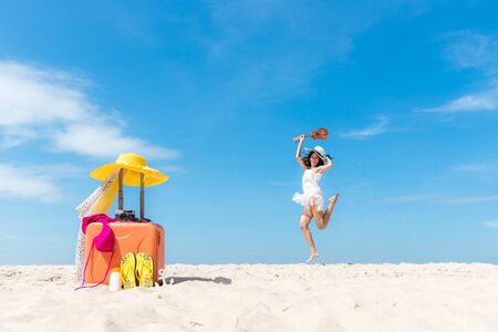 Lifestyle young woman relax on the summer beach.  Asia tourism people jumping and chill in holiday with orange luggage and sunblock items tourist for holiday,  blue sky background.  Summer Vacations Concept.の写真素材