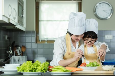 Cooking Family. Chef kid boy and mother making and leaning fresh vegetables salad for healthy eat and education.  Asian son helping make food, so happy and enjoy.  Family Lifestyle Conceptの写真素材