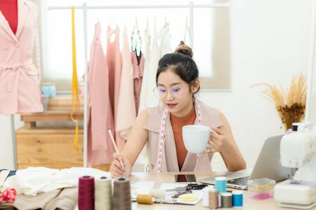 Work from home. Asian young woman fashion designer  working on her design in the showroom.  Lifestyle people Stylish tailor taking measurements on mannequin in studio.  Business small Conceptの写真素材