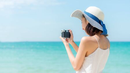 Lifestyle young woman relax on the summer beach.  Asia tourism people holding camera and take a photo on beach in holiday, blue sky background.  Summer Vacations Concept. の写真素材