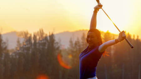 Golfer woman cheerful happy and relax with a golf in the golf club in the sunny and evening sunset time.  Golfer sport course golf ball fairway in the sunny and evening sunset time. People lifestyle woman playing game golf tee of on the green grass. Healthy and Sport outdoorの写真素材