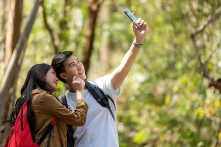 Tourist and traveler asian couple backpack enjoy happy take a photo selfie in the jungle forest nature park . Traveler going camping and explore outdoors destination leisure.の写真素材