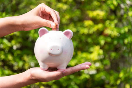 Close up hands holding piggy and putting a coin into piggy bank for future life. Investment and Saving Concept.の写真素材