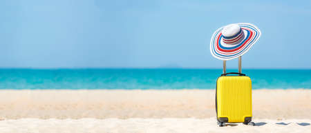 Summer traveling and tourism planning with yellow suitcase luggage with big hat fashion in the sand beach. Travel in the holiday, blue sky and beach background. Summer and Travel Concept, copy space for bannerの写真素材