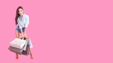 Asian smiling woman so happy with her shopping in casual clothing with shopping bags on the wall pink background, Lifestyle Concept.の写真素材