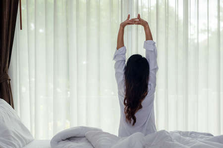 Asian women waking up stretching and raise arms in bed room at home. Young people early morning time and sunny day. Lifestyle Conceptの写真素材