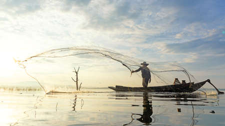 Fisherman action when fishing net on lake in the sunshine morning outdoors on the boat. Agriculture Industry, Thailandの写真素材