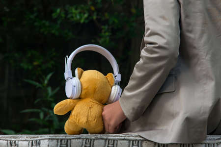 Lonely boy sitting, with his teddy bear in the park.  Teddy bear toy wearing headphones and listening music in holiday. Lifestyle Concept.の写真素材