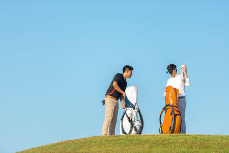 Group golfer asian two man approach on the tee off for swing and hitting golf ball and looking fairway in course. Hobby in holiday and vacations in sunny morning day on club golf.  Lifestyle, and sport Concept.の写真素材
