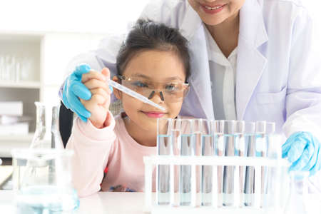 Asian children analyzing study evaluating microscope with scientist. Health care researchers doing some research with dropper chemical testing and working in life science laboratoryの写真素材