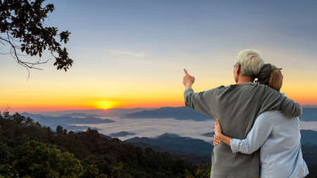 Asian Lifestyle senior couple hug and pointing the mountain field during mist sunrise nature.  Old people happy in love romantic and relax time.Â  Tourism family elderly retirement travel in attraction place tourist travel leisure and destination.の写真素材