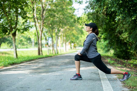 Healthy woman warming down stretching her legs in the road outdoor. Asian runner woman workout...
