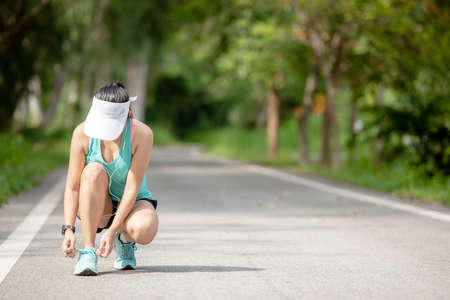 Runner young asia woman tying laces of running shoes before jogging through the road in the workout nature park.  Weight Loss and Healthy Conceptの写真素材