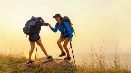 Group young women of hikers walking with backpack on a mountain at sunset.  Traveler going camping...