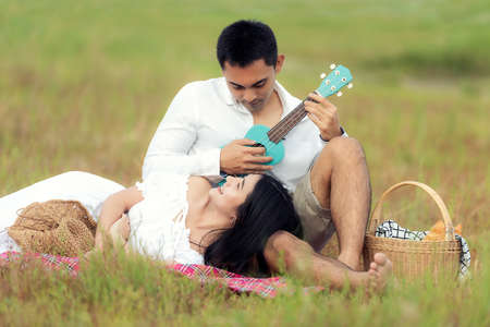 Lifestyle couple happy honeymoon in sunny time. Asian young couple sitting picnic and relax in the meadow and field near river and mountain in holiday.  Romantic and In love.  Lifestyle conceptの写真素材