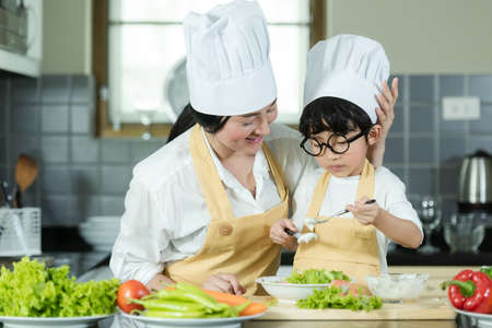 Cooking Family. Chef kid boy and mother making and leaning fresh vegetables salad for healthy eat and education.  Asian son helping make food, so happy and enjoy.  Family Lifestyle Conceptの写真素材