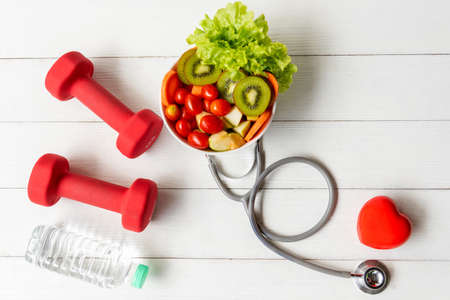 Health Care.  Fresh vegetable salad with medical stethoscope and equipment dumbbell for diet and weight loss for healthy care and protect virus,  white wooden background.  Healthy Life Conceptの写真素材