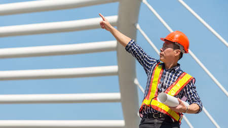 Engineer inspector construction building in the project site. Asia man architect worker holding white helmet for workers security control at city site.   Industry and Engineer Conceptの写真素材