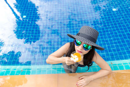 Summer time and Vacations. Women lifestyle relaxing and drinking juice orange so happy in luxury swimming pool sunbath, summer day at the beach resort in the hotel. Summer Conceptの写真素材