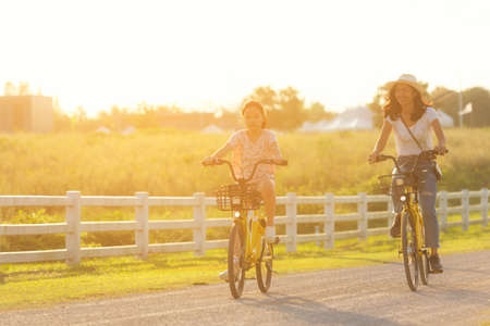 Mother and daughter with bicycling at the garden meadow in sunset near white fence.  Lifestyle Family Conceptの写真素材