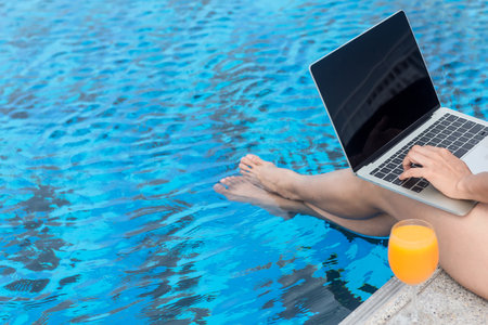 Close up and select legs.  Summer time and Vacations. Women lifestyle relaxing and working laptop in swimming pool outdoor, summer day at the beach resort in the hotel. Summer Conceptの写真素材
