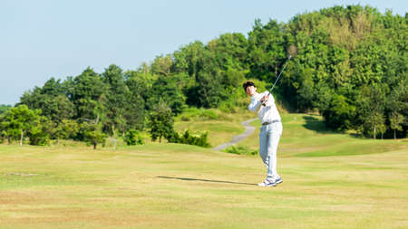 Golfer asian man swing and hitting golf ball practice at golf driving range and fairway with bag golf on multiethnic club. Lifestyle and Sport Conceptの写真素材