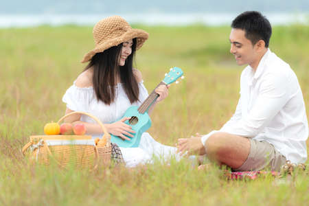 Lifestyle couple picnic and relax. People young woman and man having fun and happy playing guitar picnic in the meadow and field sunny time in holiday.  Romantic and In love. Lifestyle summer Conceptの写真素材
