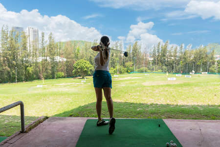 Asian golfer woman swing golf ball practice at golf driving range for relax and healthy care port. Lifestyle and Sport Concept, blue sky backgroundの写真素材