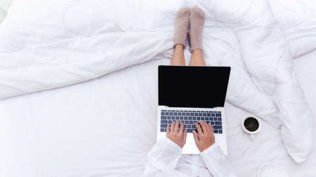 Close up legs women on white bed in the bedroom. Women working on laptop and drinking coffee in morning relax mood in winter season. Lifestyle Concept.の写真素材