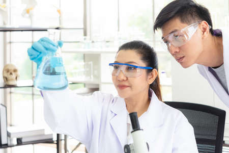 Team work asian woman and man Scientists analyzing study data and evaluating microscope success for...