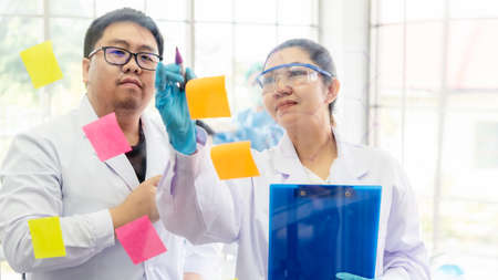 Team work asian woman and man Scientists analyzing study data and evaluating microscope success for...