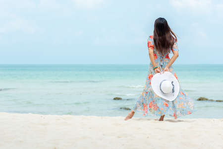 Summer Trips.  Lifestyle woman wearing fashion summer walking and holding big hat on the sandy ocean beach. Happy people truist travel enjoy and relax vacation.  Lifestyle and Travel Summer Concept.の写真素材