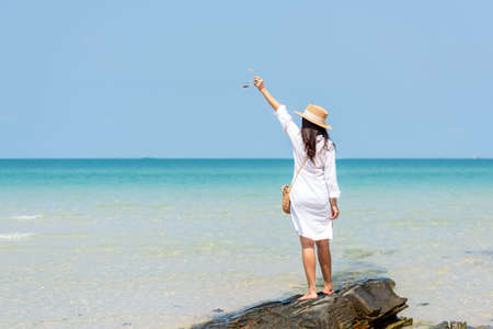 Summer vacations. Lifestyle woman relax and chill on beach background.  Asia happy young people with white dress raise arm on the wave sea, summer trips walking enjoy  tropical beach. Lifestyle and Travel Conceptの写真素材