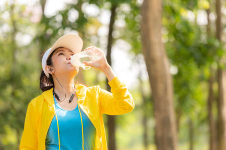 Healthy athletic asia woman is drinking pure water from the bottle refreshing herself after exercise in the nature park. Healthy and Lifestyle Conceptの写真素材