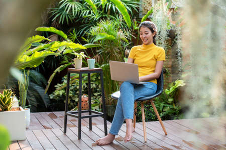 Young people work from home with laptop and drinking coffee in garden nature at home. Asia woman meeting conference connect online with office.  Business and Technology Conceptの写真素材