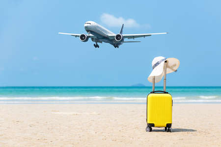 Summer traveling and planning with yellow suitcase luggage with big white hat fashion on the sand beach. Travel in the holiday, airplane and blue sky and beach background. Summer and Travel Conceptの写真素材