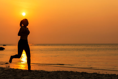 Silhouette athletic woman jogging and relax and freedom on sand beach. People running and workout in sunset background. Lifestyle and Healthy Concept.の写真素材