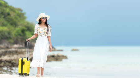 Happy traveler and tourism young women travel summer on the beach.Â  Asian smiling people with white dress holding yellow suitcase walking and relax outdoor for destination  leisure trip travel in holidayの写真素材