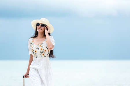 Summer vacations. Lifestyle woman relax and chill on beach.  Asian happy young people wearing white dress fashion and holding suitcase  in summer trips enjoy  tropical beach. Lifestyle and Travel Concept.の写真素材