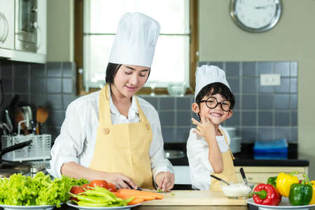 Cooking Family. Chef kid boy and mother making and leaning fresh vegetables salad for healthy eat and education.  Asian son helping make food, so happy and enjoy.  Family Lifestyle Conceptの写真素材