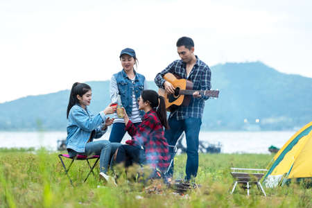 Camping outdoor. Group  friends holding bottle alcohol drinking and camping leisure and destination travel in sunset. Tourism relax and travel near river in holiday.の写真素材