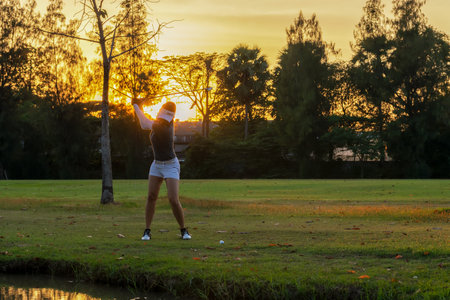 Golfer sport course golf ball fairway. People lifestyle woman playing game golf and swing golf ball go on green grass sunset background.Â  Asia female player game shot in summer.Â  Healthy and Sport outdoorの写真素材